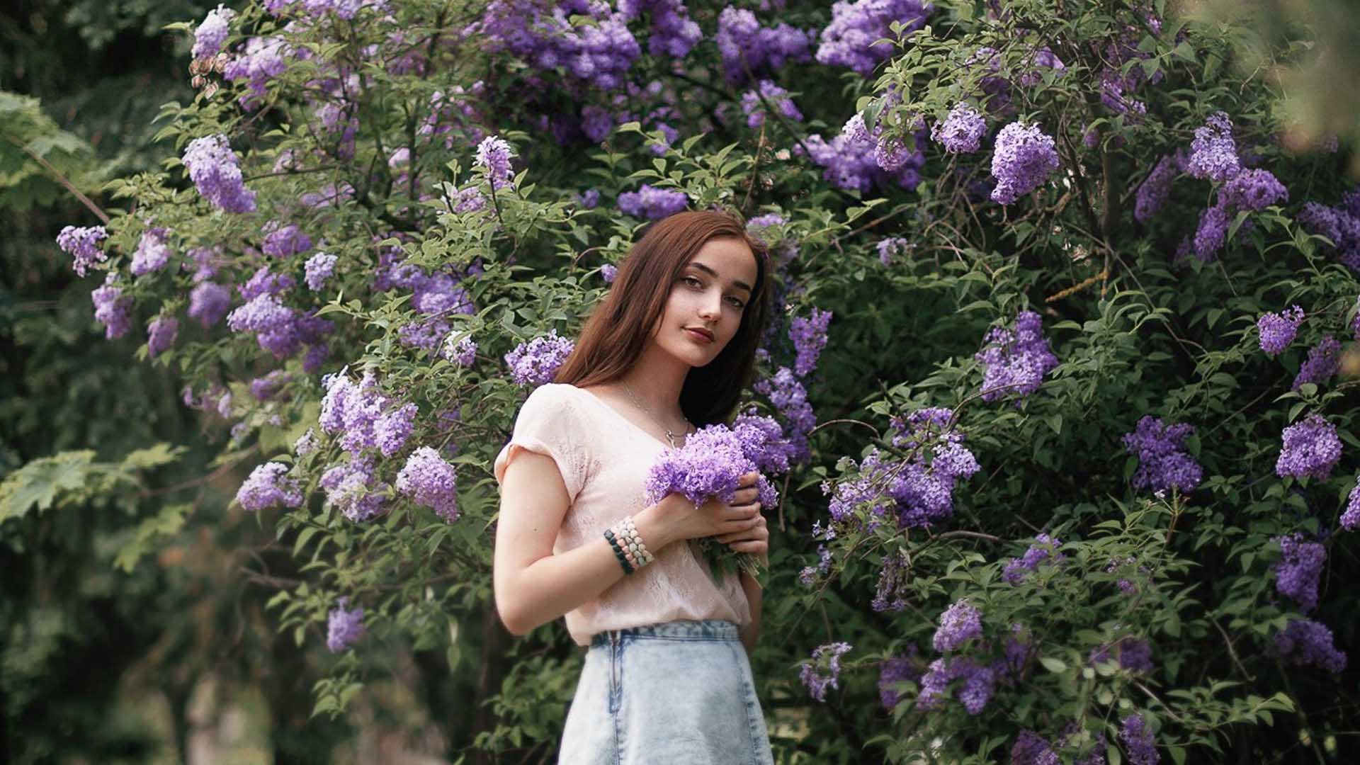 Girl Model With Purple Flowers Is Wearing Light Pink Tops And Jeans Skirt Standing Near Flowers Trees HD Girls