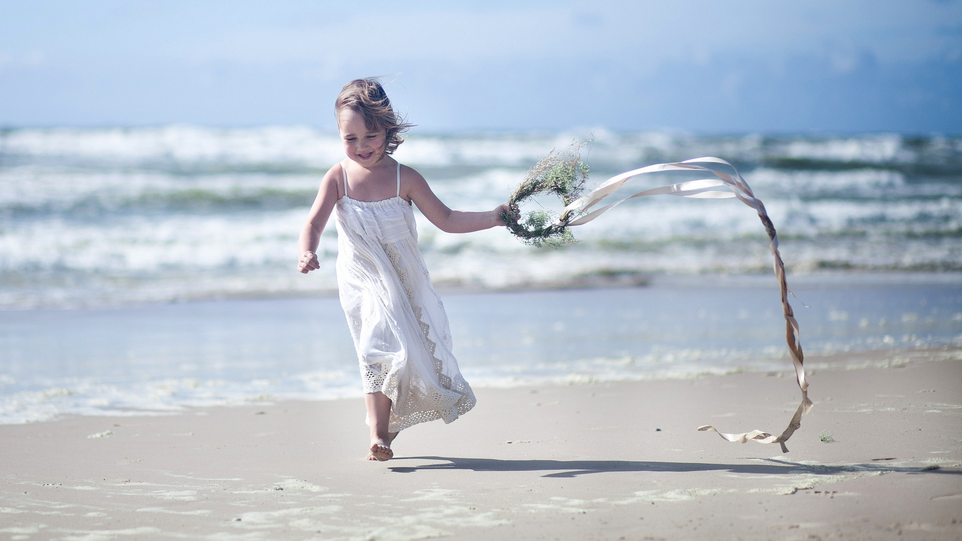 Happy Smiley Little Girl Is Running On Beach Sand Wearing White Dress With Wreath HD
