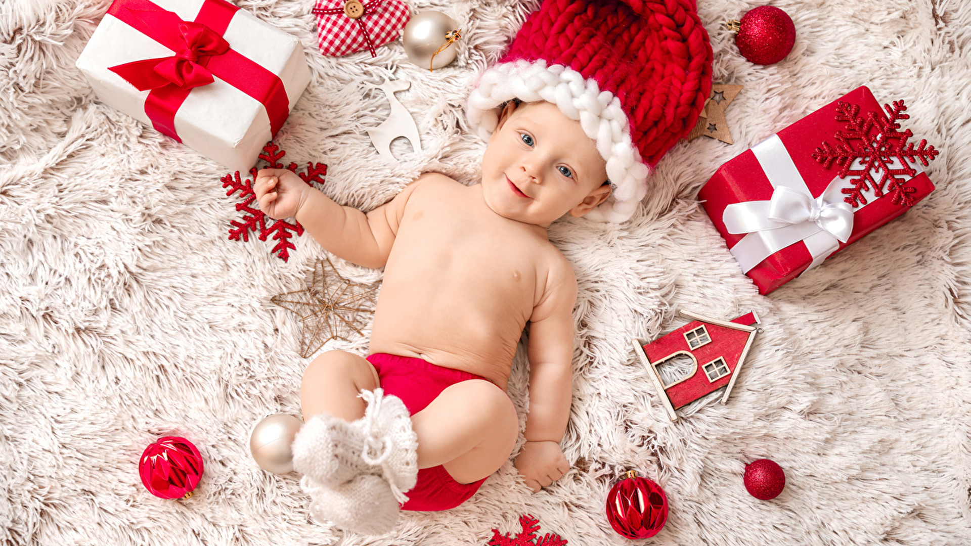 Beautiful Smiley Infant Is Lying Down On White Fur Cloth Wearing Red White Woolen Knitted Cap HD