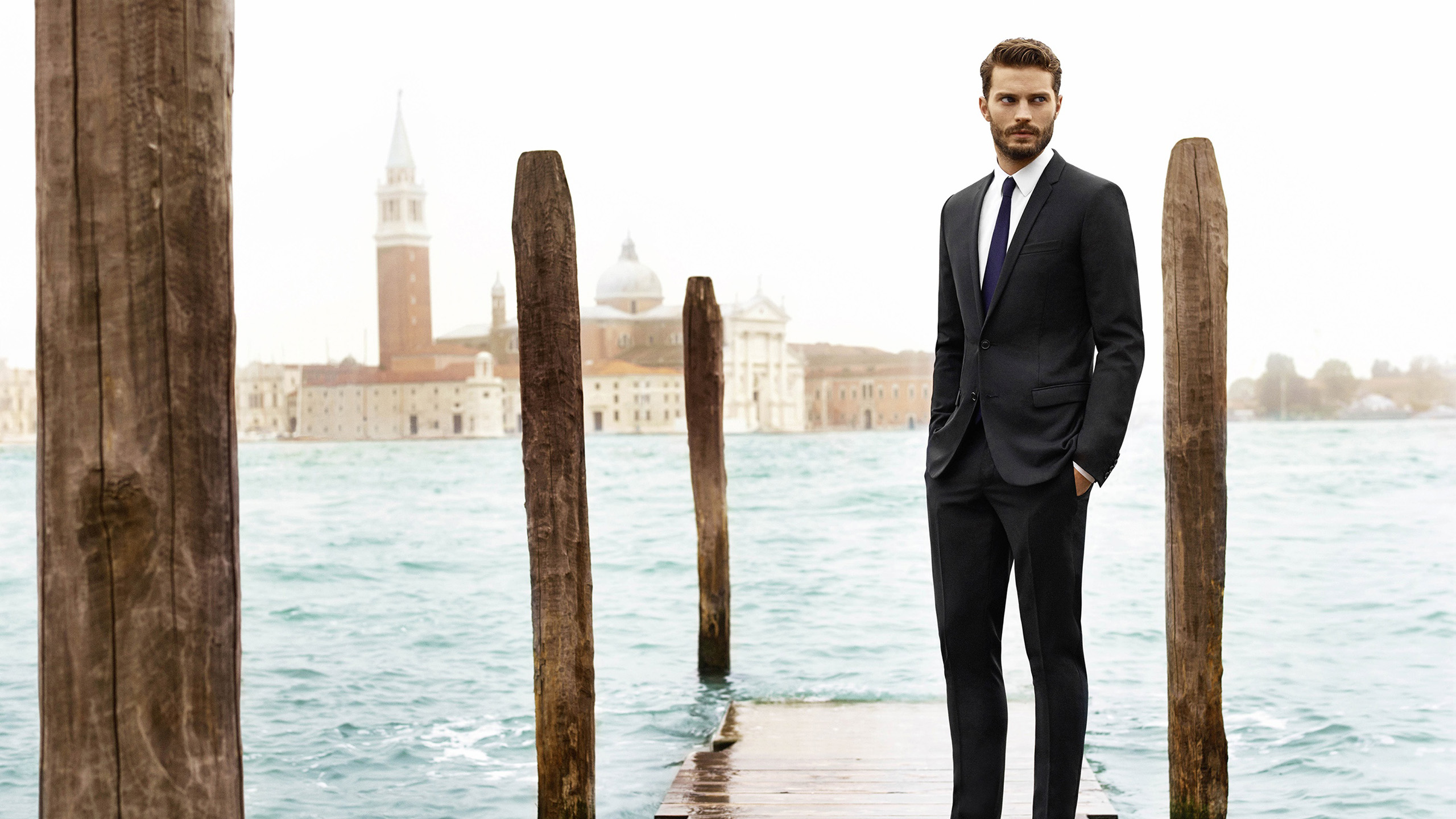 Jamie Dornan Is Standing On Wooden Dock Wearing Black Coat Suit In River Wallpaper HD Boys